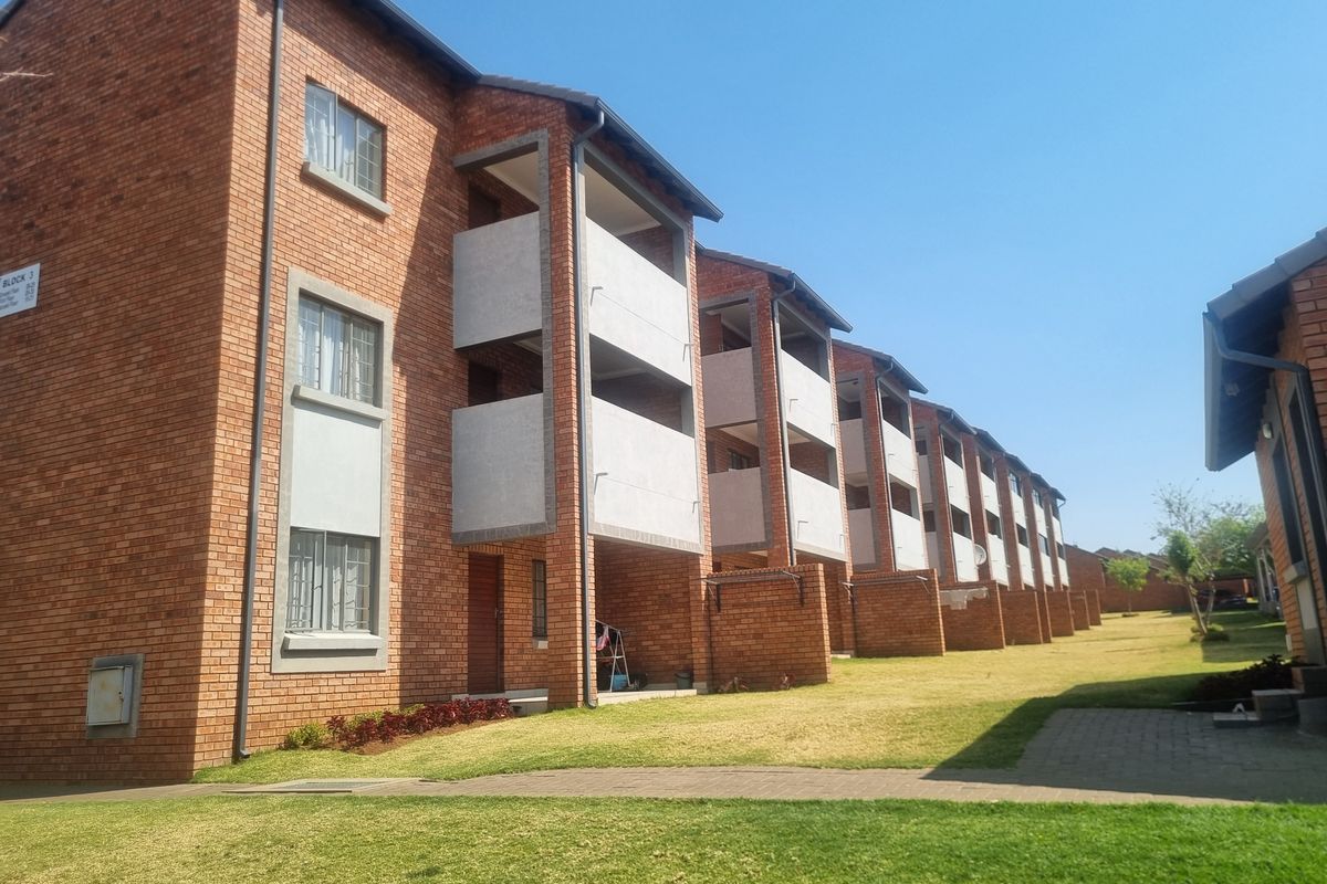 A view of the rear elevation of a multi-story apartment block featuring face brick construction, private balconies, and well-maintained communal lawn areas.