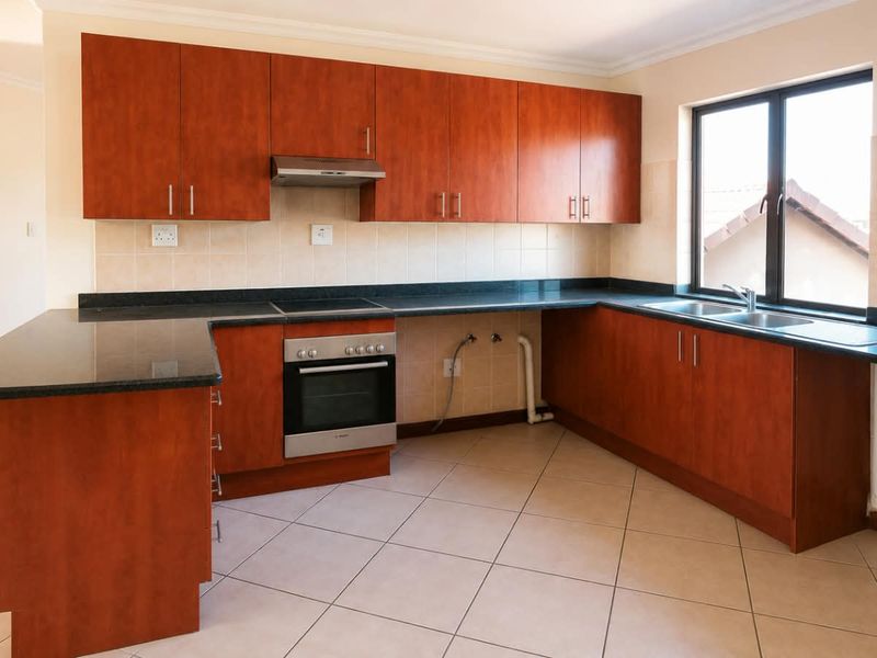 A functional kitchen featuring cherry-wood cabinetry, granite countertops, built-in oven and hob, and tiled flooring with a double basin sink.