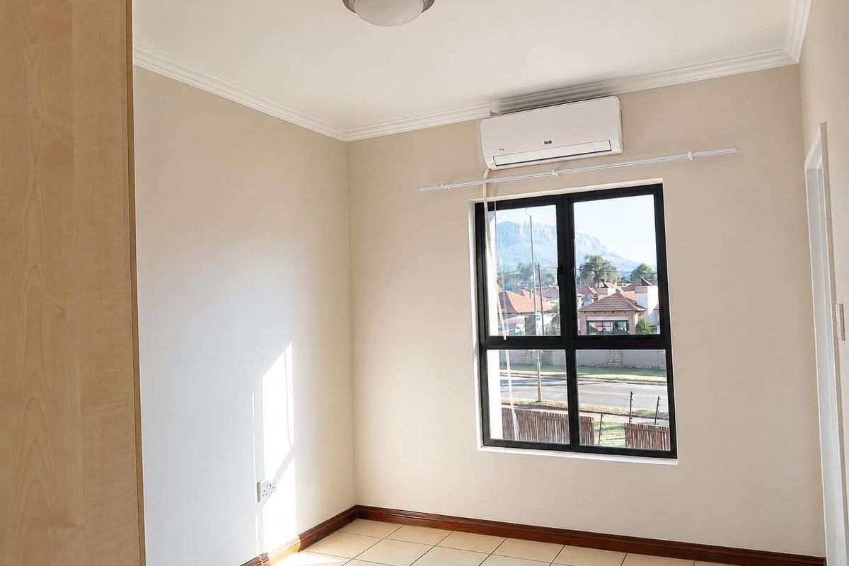 A bright, empty bedroom featuring tiled flooring, a built-in cupboard, and a wall-mounted air conditioning unit with views of the surrounding neighbourhood.
