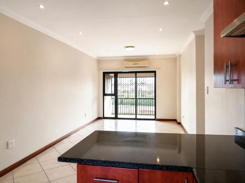 An open-plan living area featuring tiled floors, recessed lighting, and a kitchen with granite countertops, leading to a balcony through a secure sliding door.