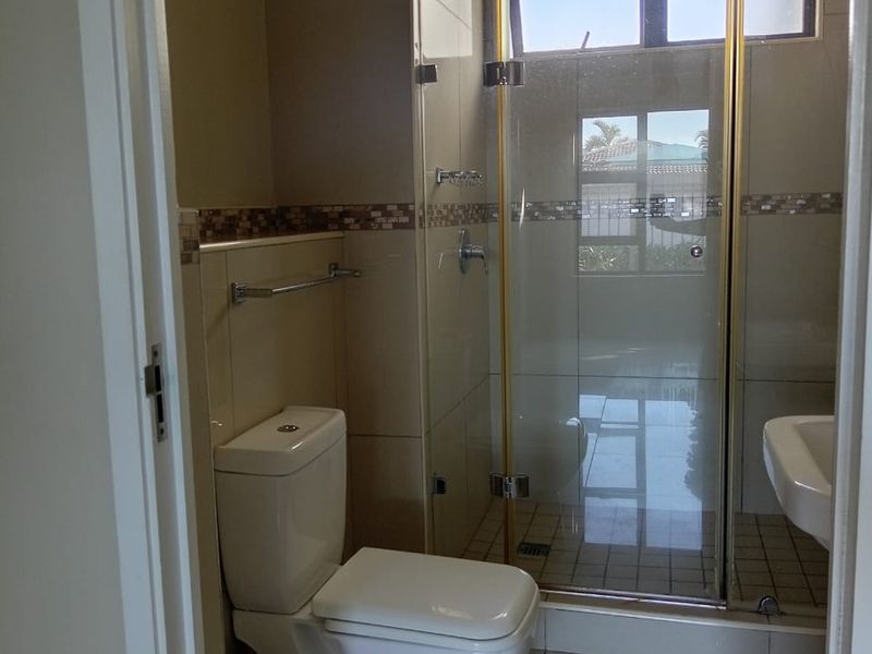 A clean, functional bathroom featuring a glass-enclosed shower, wall-mounted basin, and modern tiled finishes.