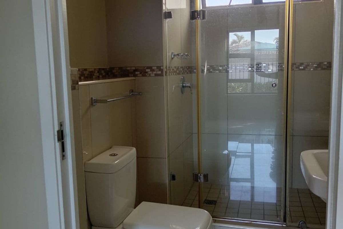 A clean, functional bathroom featuring a glass-enclosed shower, wall-mounted basin, and modern tiled finishes.