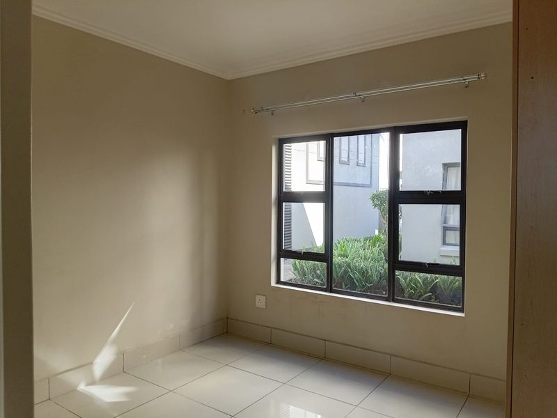 A bright, empty bedroom featuring neutral tiled flooring, large aluminium-framed windows, and clean wall finishes, ready for personalization.