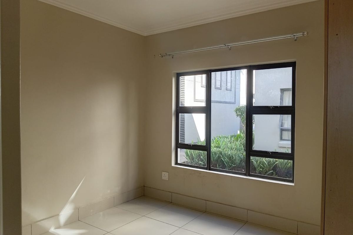 A bright, empty bedroom featuring neutral tiled flooring, large aluminium-framed windows, and clean wall finishes, ready for personalization.