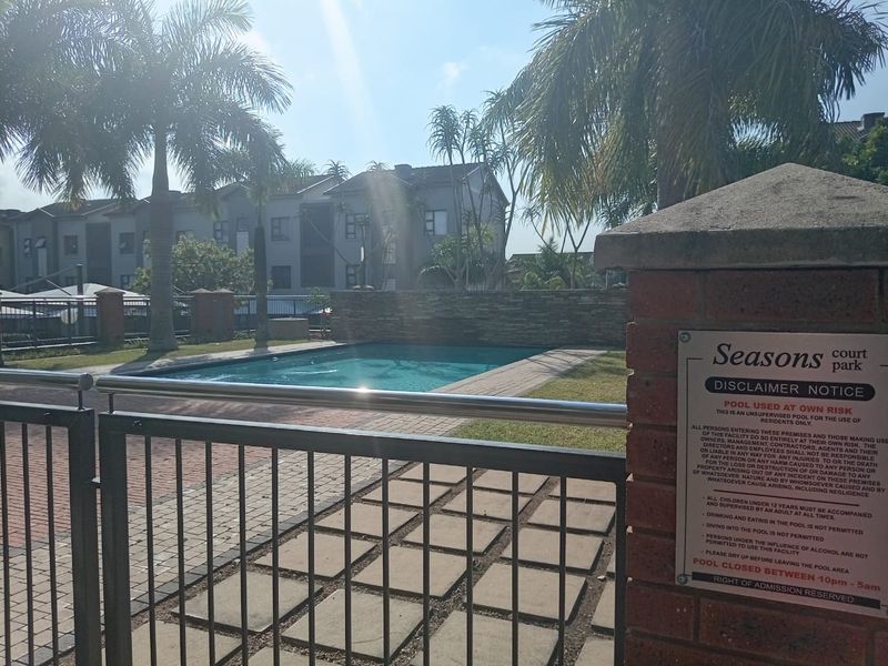 A well-maintained communal swimming pool area featuring brick paving, a stone feature wall, and secure metal gate access within the apartment complex.