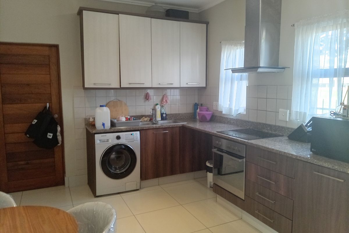 A functional kitchen featuring two-tone cabinetry, granite countertops, a built-in oven with extractor fan, and tiled flooring with integrated laundry plumbing.
