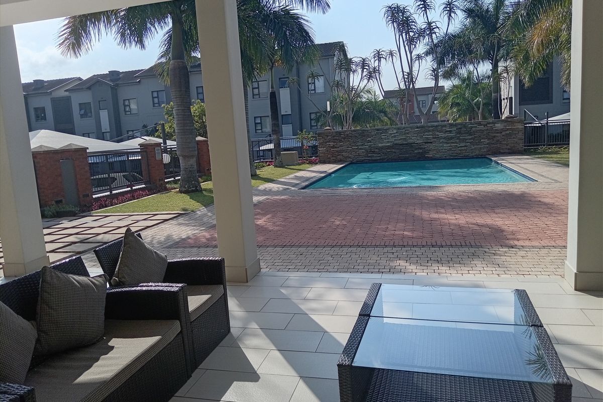 A covered patio area overlooking a communal swimming pool and landscaped garden within an apartment complex.