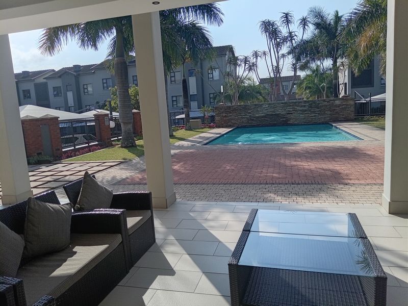 A covered patio area overlooking a communal swimming pool and landscaped garden within an apartment complex.