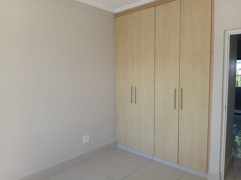 A clean, empty bedroom featuring light-toned built-in cupboards and neutral tiled flooring, offering a versatile space ready for personalization.