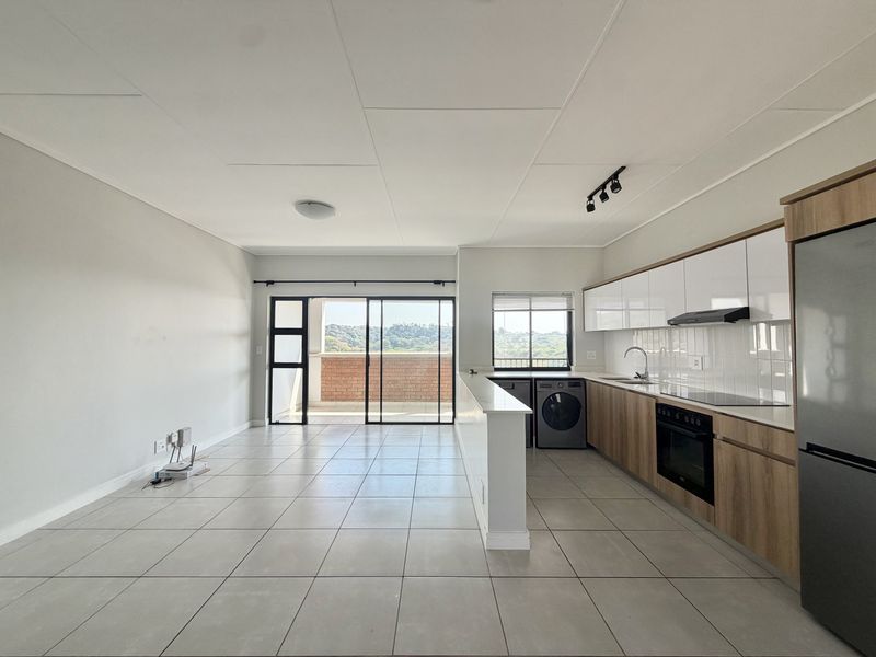 Modern open-plan kitchen and living area featuring sleek cabinetry, integrated appliances, tiled floors, and direct access to a private balcony with scenic views.