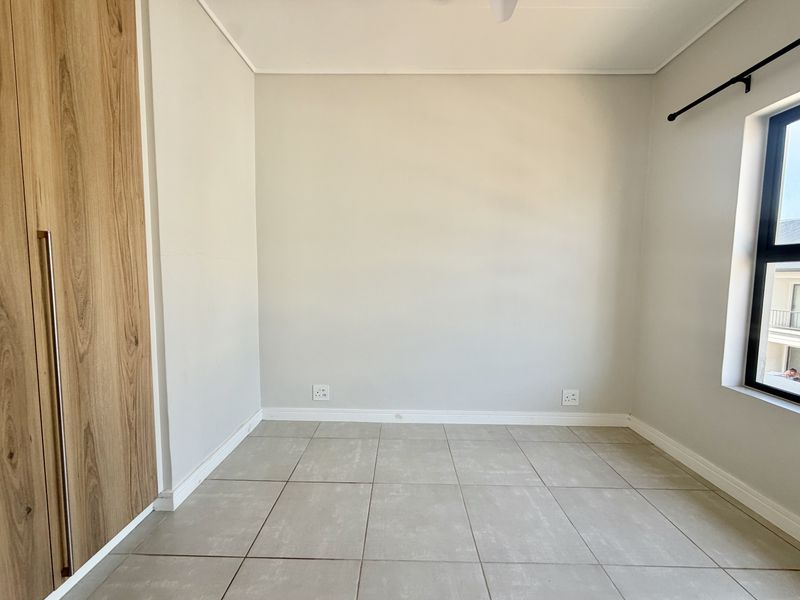 A clean, empty bedroom featuring neutral tiled flooring, a modern built-in wardrobe, and ample natural light from the window.