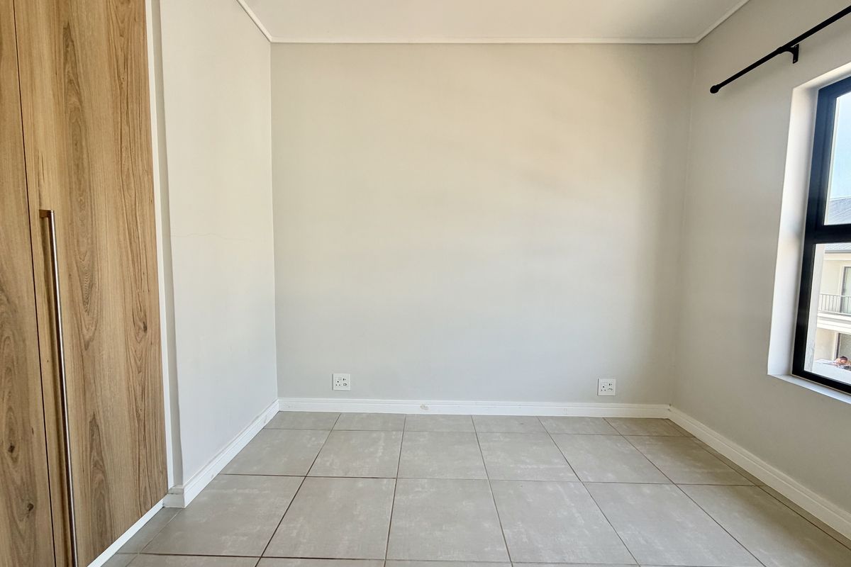 A clean, empty bedroom featuring neutral tiled flooring, a modern built-in wardrobe, and ample natural light from the window.