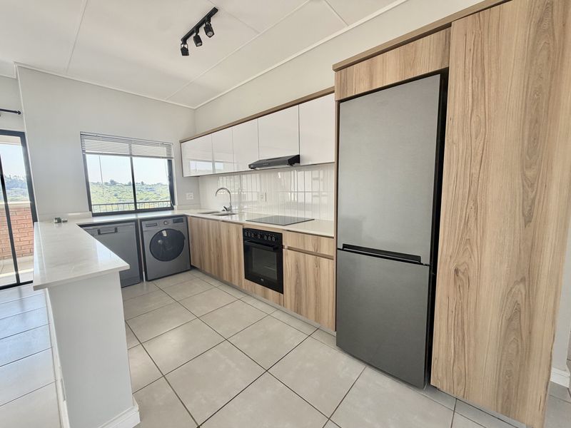 Modern kitchen featuring wood-grain and white cabinetry, stone countertops, integrated appliances, and tiled flooring with ample natural light.
