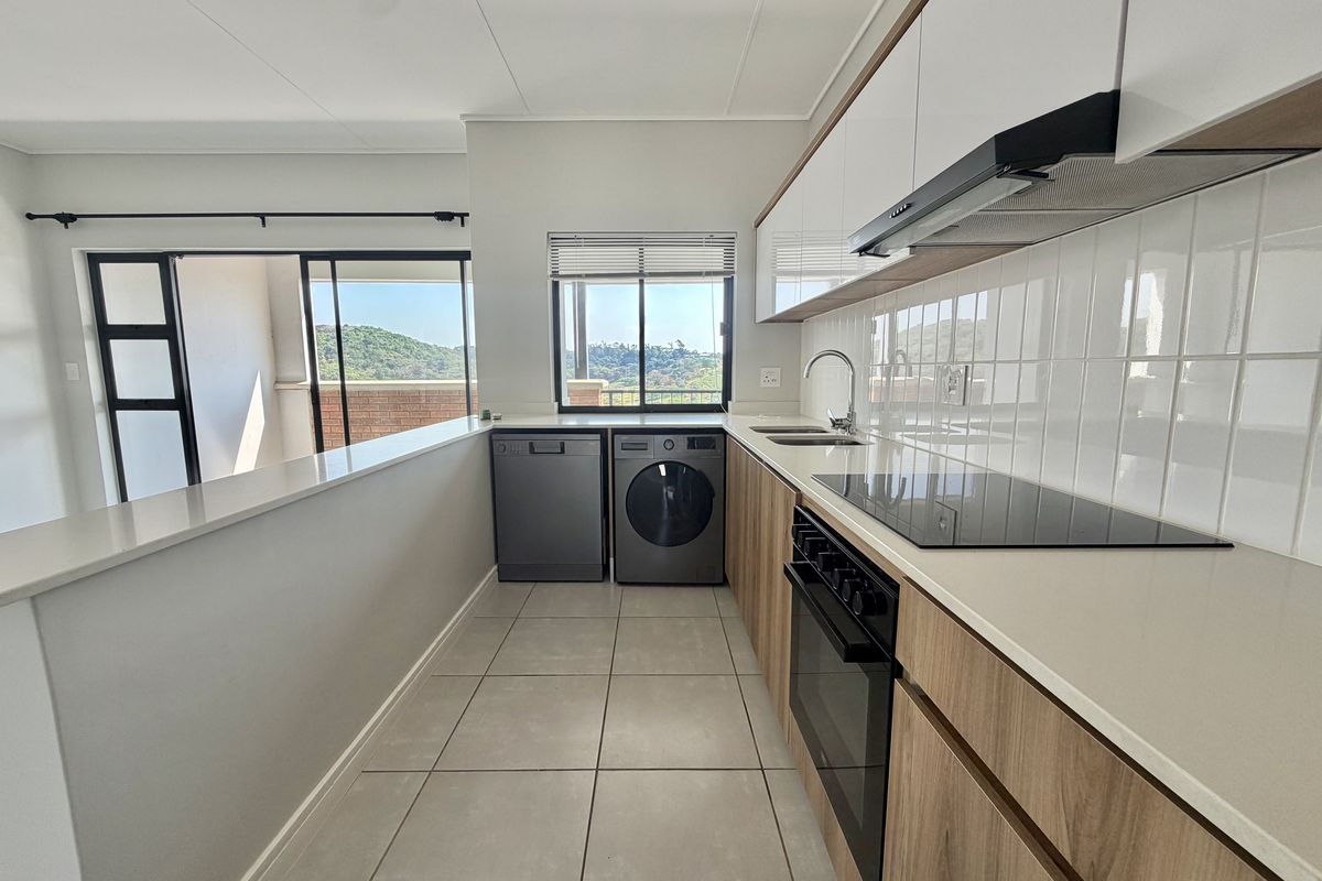 Modern kitchen featuring sleek wood-finish cabinetry, stone countertops, integrated appliances, and tiled flooring, with an open-plan layout and views of the surrounding landscape.