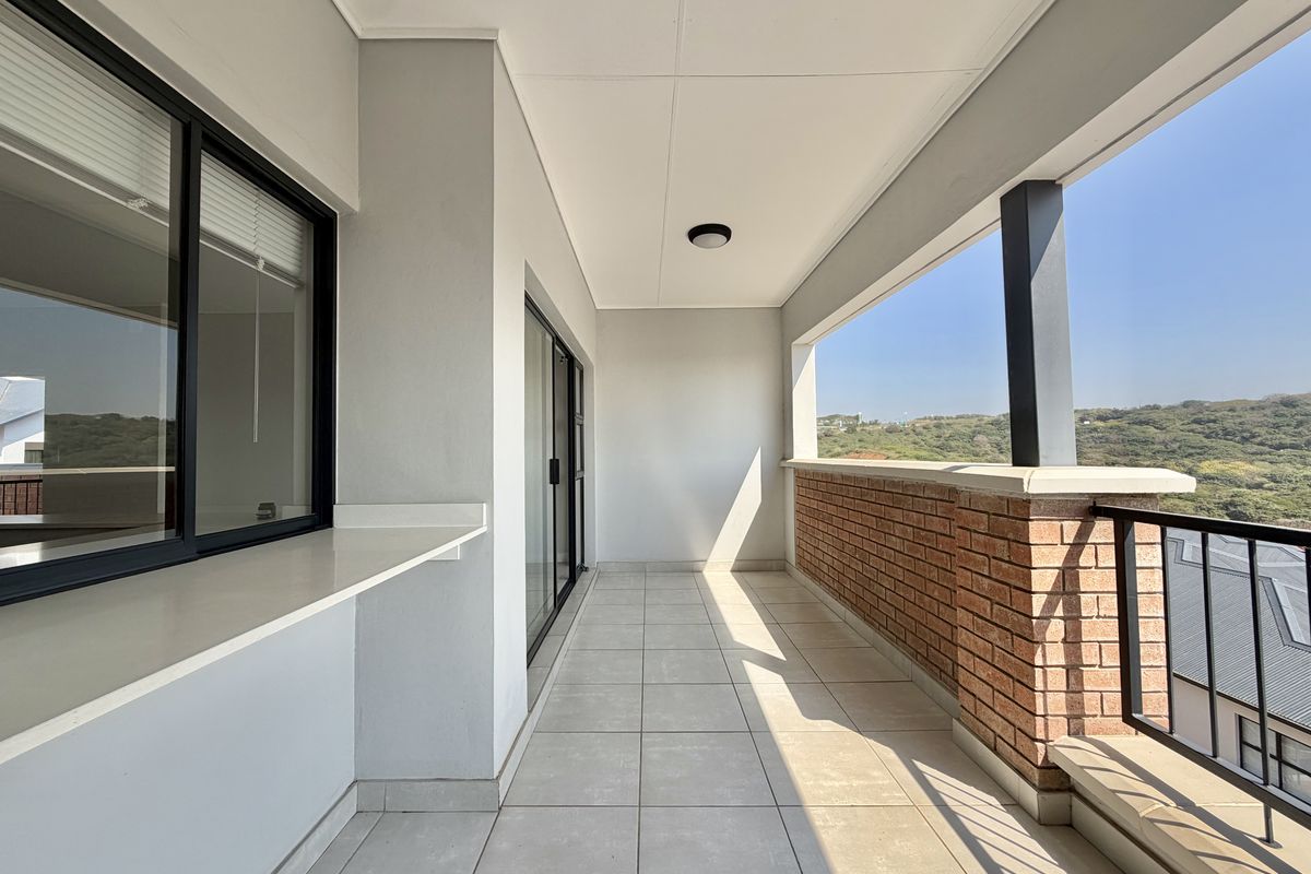 A spacious, well-maintained balcony featuring tiled flooring, a brick balustrade with metal railing, and scenic views.