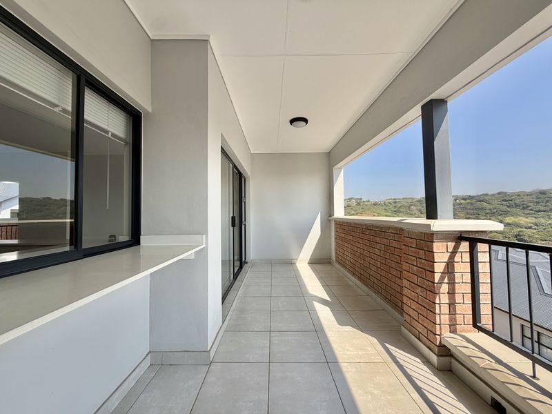 A spacious, well-maintained balcony featuring tiled flooring, a brick balustrade with metal railing, and scenic views.