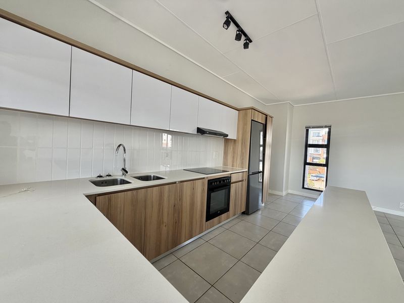Modern kitchen featuring sleek wood-tone cabinetry, white stone countertops, integrated appliances, and tiled flooring in a clean, contemporary open-plan layout.