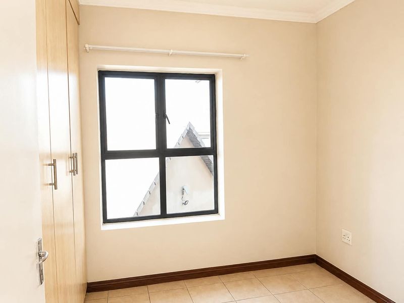 A clean, empty bedroom featuring neutral walls, tiled flooring, and built-in wooden cupboards with modern hardware.