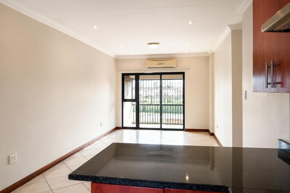 An open-plan living area featuring tiled floors, recessed lighting, and a kitchen with granite countertops, leading to a balcony through a secure sliding door.