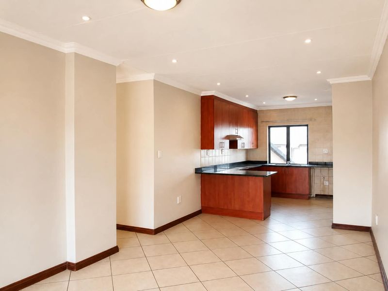 An open-plan living and kitchen area featuring tiled flooring, wooden cabinetry, granite countertops, and recessed lighting in a neutral, well-maintained space.