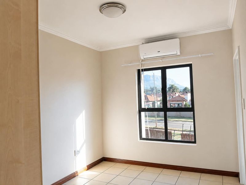 A bright, empty bedroom featuring tiled flooring, a built-in cupboard, and a wall-mounted air conditioning unit with views of the surrounding neighbourhood.