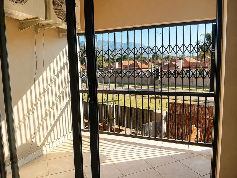 A covered balcony featuring tiled flooring, a security gate, and an external air conditioning unit, offering views of the surrounding neighborhood.