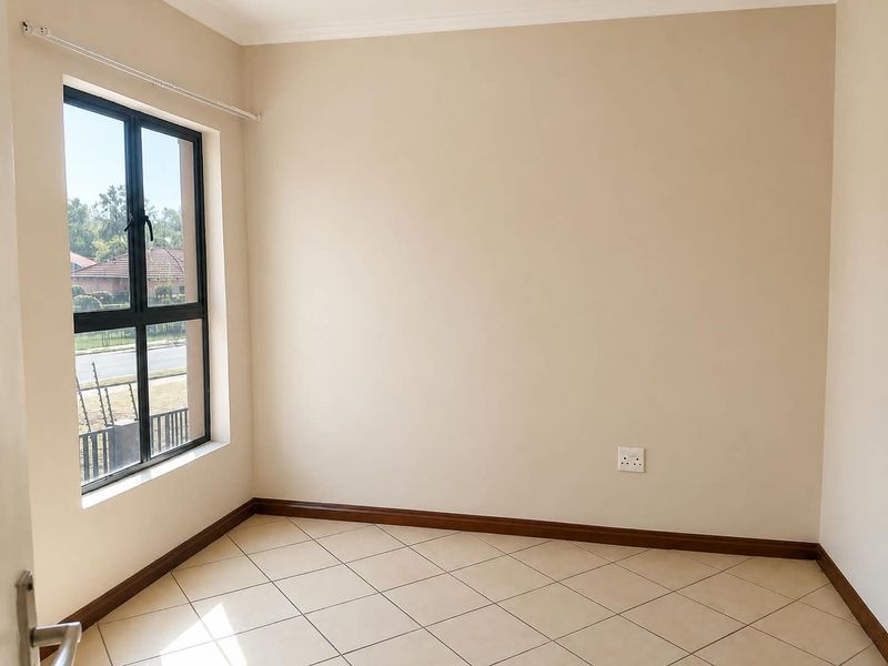 A bright, empty bedroom featuring neutral walls, tiled flooring, and a large window providing natural light.
