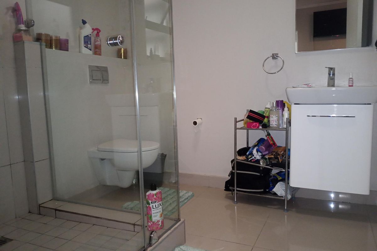 A functional bathroom featuring a glass-enclosed shower, wall-hung toilet, and a modern vanity basin with a wall-mounted mirror.