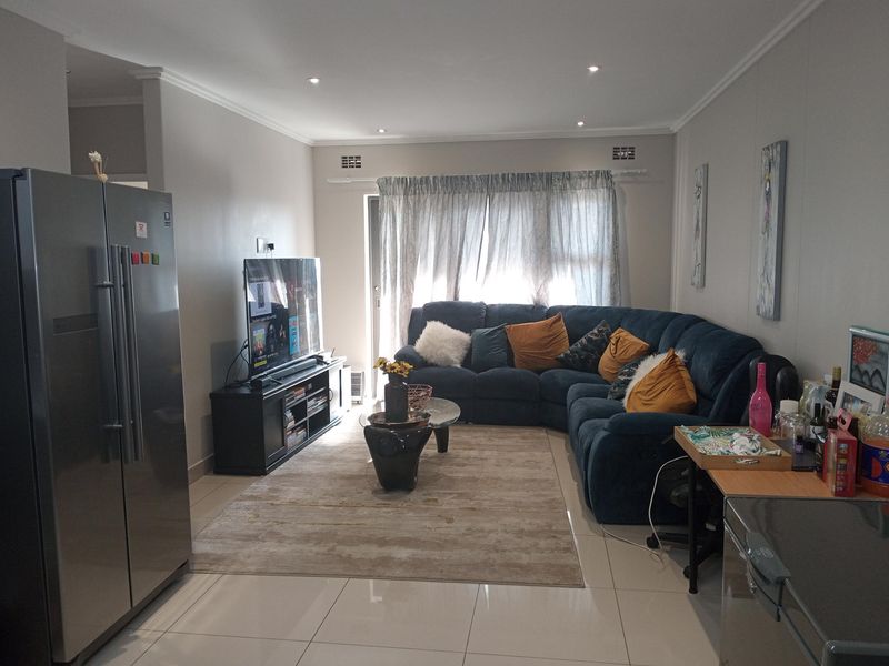 A well-maintained living room featuring neutral tiled flooring, recessed downlighting, and a sliding glass door providing natural light.