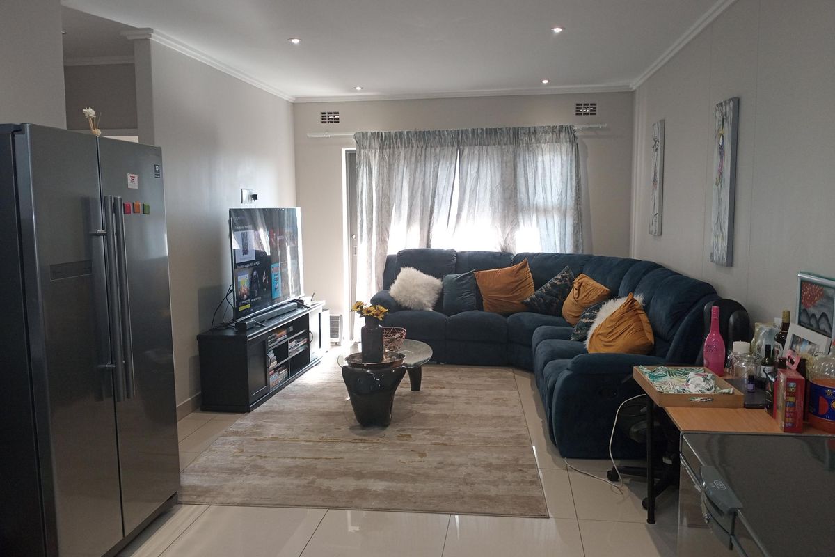 A well-maintained living room featuring neutral tiled flooring, recessed downlighting, and a sliding glass door providing natural light.