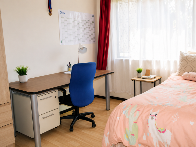 A well-lit bedroom featuring laminate flooring, a built-in wardrobe, and a window fitted with security bars.