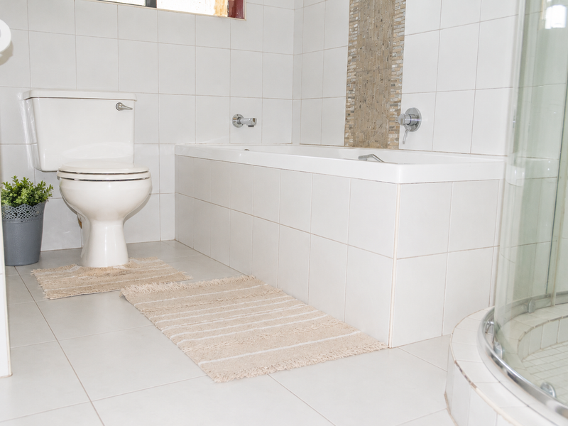 A clean, functional bathroom featuring a white bathtub, a separate shower enclosure, and a toilet, finished with neutral wall and floor tiles.