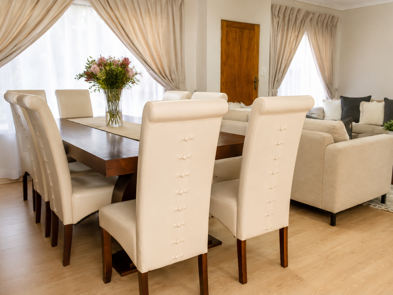 An open-plan living and dining area featuring light laminate flooring, neutral walls, and large windows with curtains, creating a bright and cohesive living space.