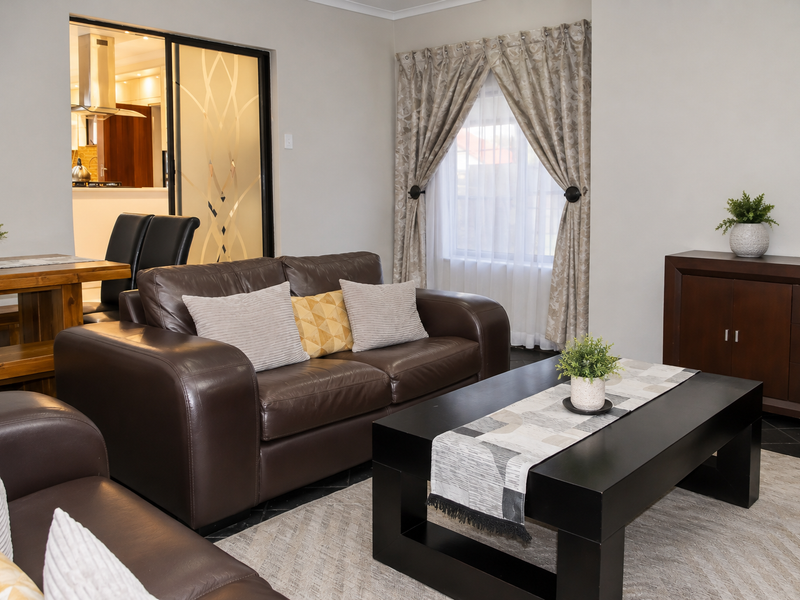 Open plan living area featuring a view into the kitchen through a decorative sliding glass door, with neutral walls and tiled flooring.