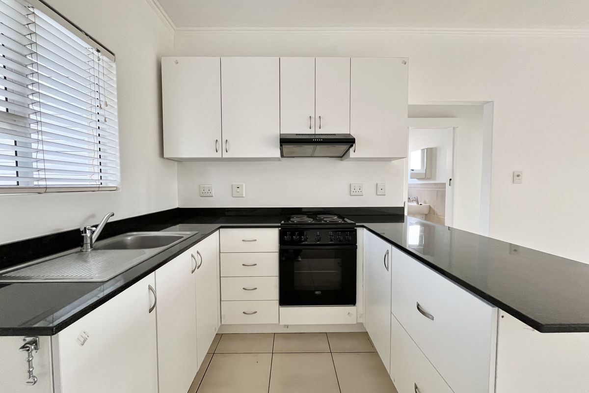 A clean, functional kitchen featuring white cabinetry, black granite countertops, a built-in electric stove with extractor fan, and tiled flooring.