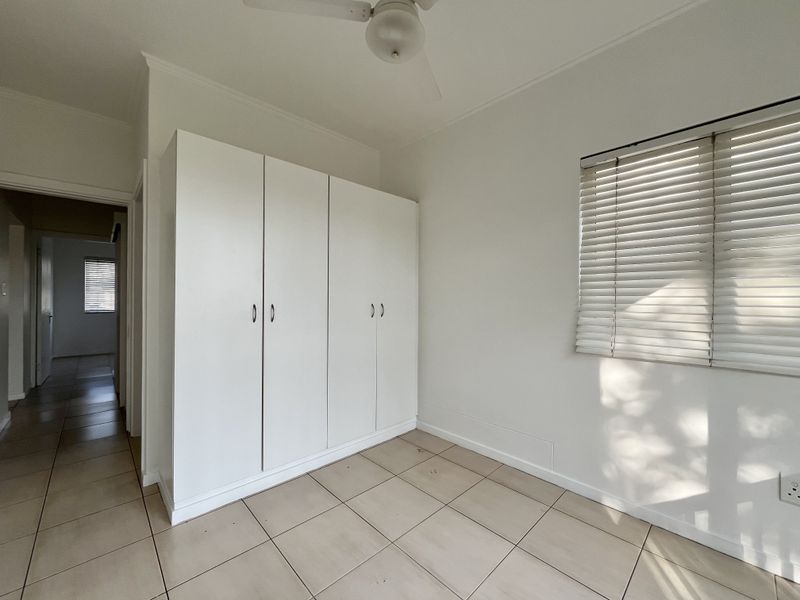 An empty bedroom featuring tiled flooring, a built-in wardrobe, a ceiling fan, and venetian blinds.