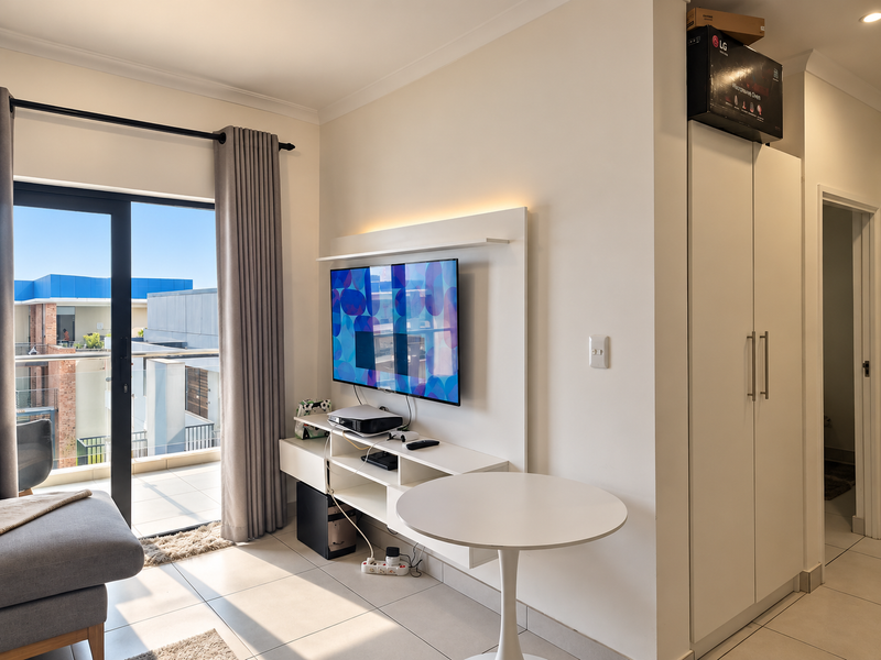 Modern living area featuring a built-in media console, tiled flooring, and a sliding glass door providing access to a private balcony.