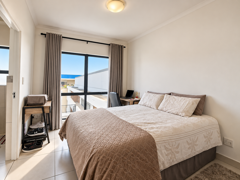 A well-lit bedroom featuring tiled flooring, a large window with curtain tracks, and neutral wall finishes, providing a comfortable and functional living space.
