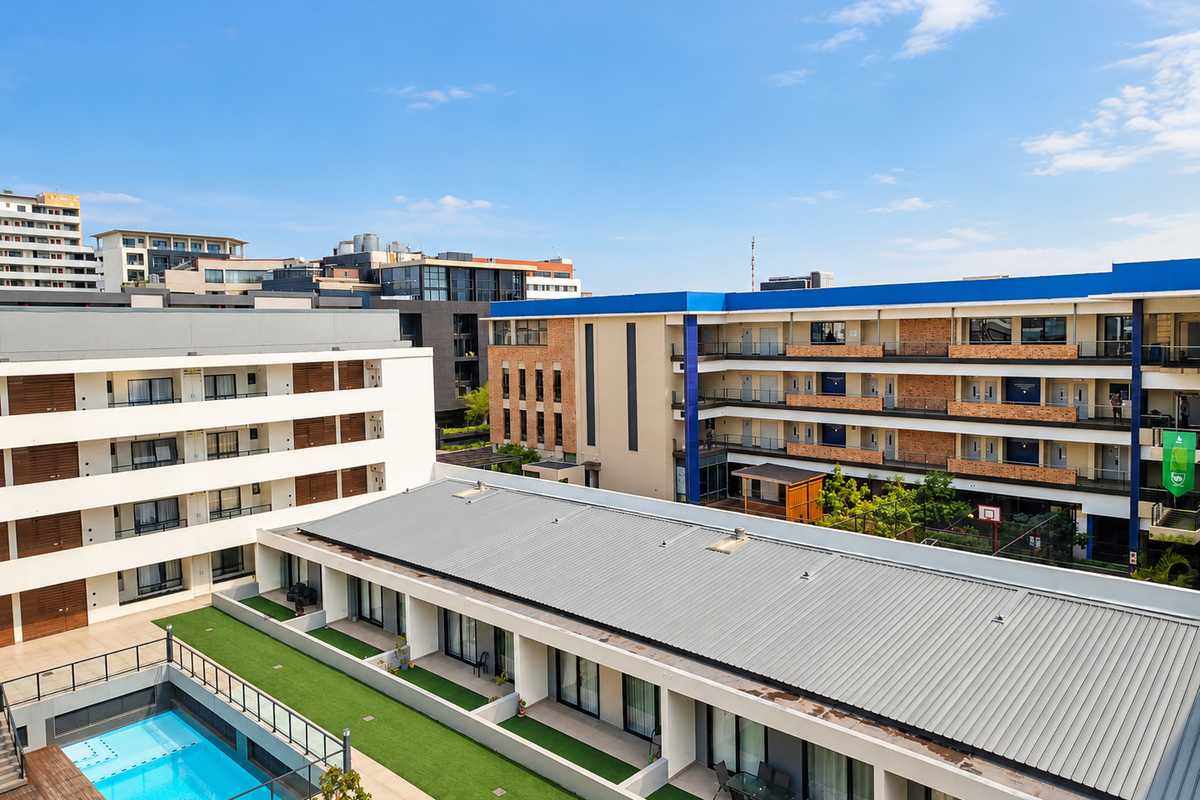 Aerial view of an apartment complex featuring a swimming pool, landscaped courtyard, and modern multi-story residential buildings with balconies.