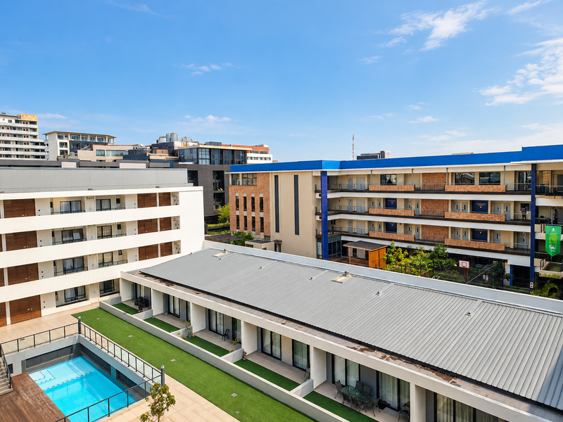Aerial view of an apartment complex featuring a swimming pool, landscaped courtyard, and modern multi-story residential buildings with balconies.
