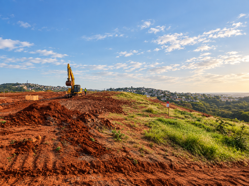 A wide-angle view of a vacant residential plot under development, featuring cleared earth and distant coastal landscape views.