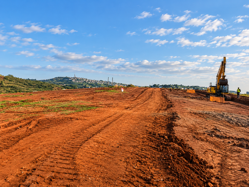 A wide-angle view of a cleared residential development site featuring ongoing earthworks and distant hillside views.
