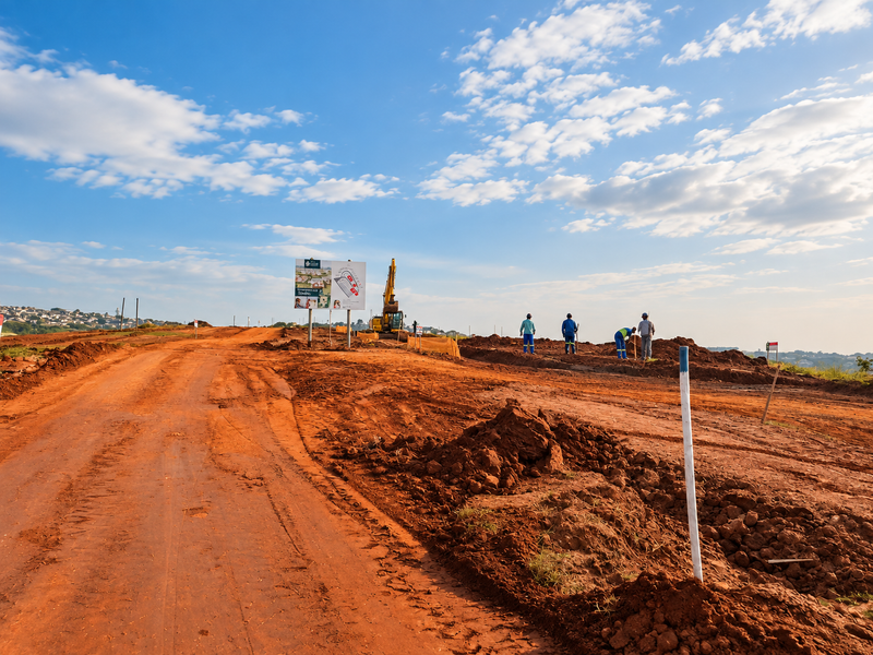 A view of a residential development site under construction with earthworks, unpaved access roads, and site signage visible.