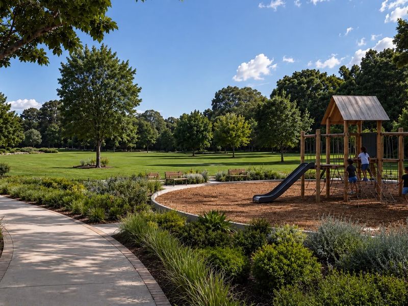 A well-maintained communal garden area featuring a paved walkway, landscaped garden beds, and a children's playground set within a spacious green park.
