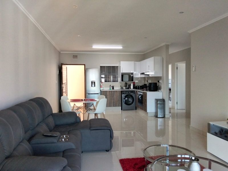 An open-plan living and kitchen area featuring modern cabinetry, integrated appliances, tiled flooring, and recessed lighting, creating a functional and cohesive living space.