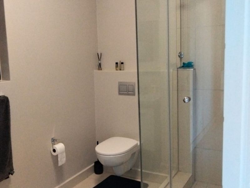 Modern bathroom featuring a wall-mounted toilet with a concealed cistern and a glass-enclosed shower with tiled finishes.