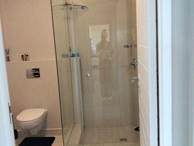 A modern bathroom featuring a wall-mounted toilet, a glass-enclosed shower, and neutral floor tiling.