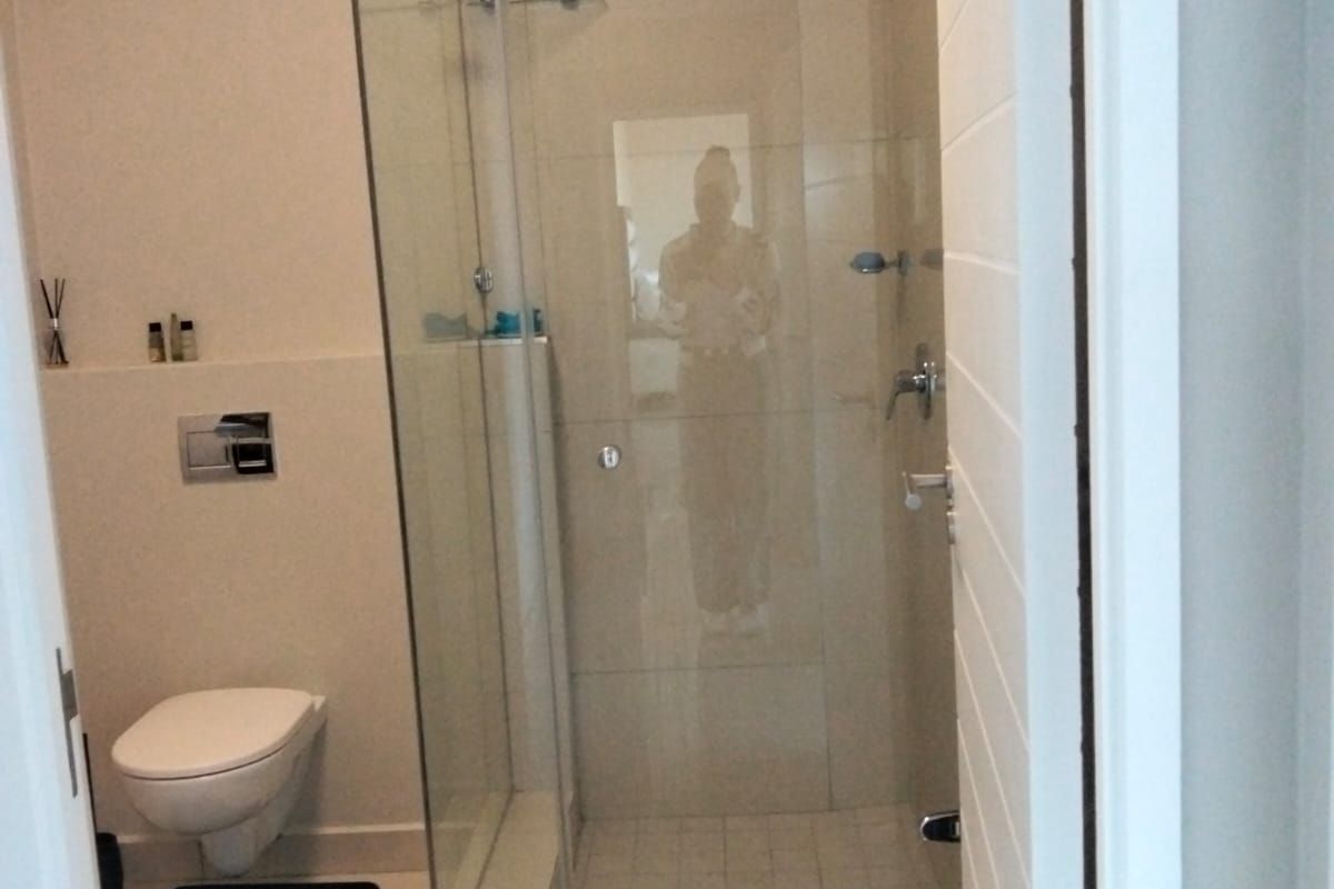 A modern bathroom featuring a wall-mounted toilet, a glass-enclosed shower, and neutral floor tiling.