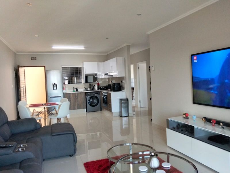 An open-plan living and kitchen area featuring modern cabinetry, integrated appliances, tiled flooring, and recessed lighting in a well-maintained apartment setting.