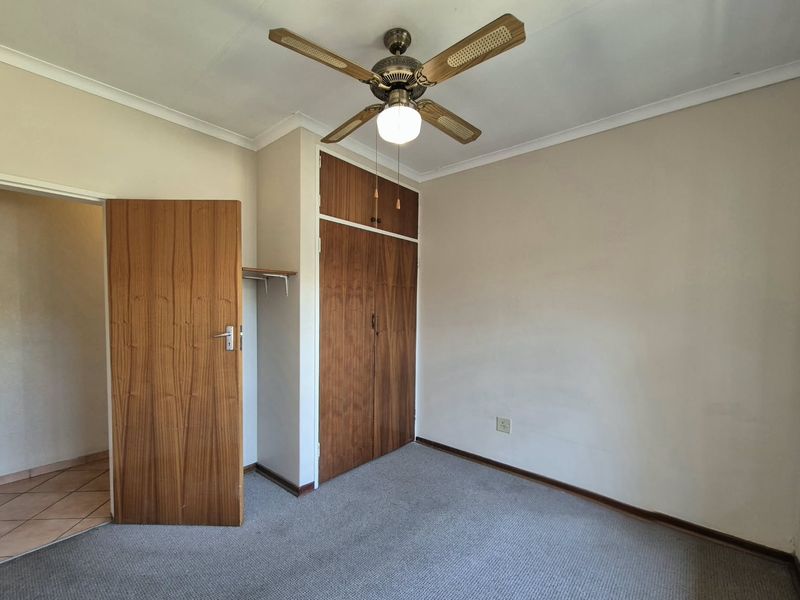 A vacant bedroom featuring built-in wooden cupboards, a ceiling fan, and carpeted flooring, offering a neutral space ready for personalization.